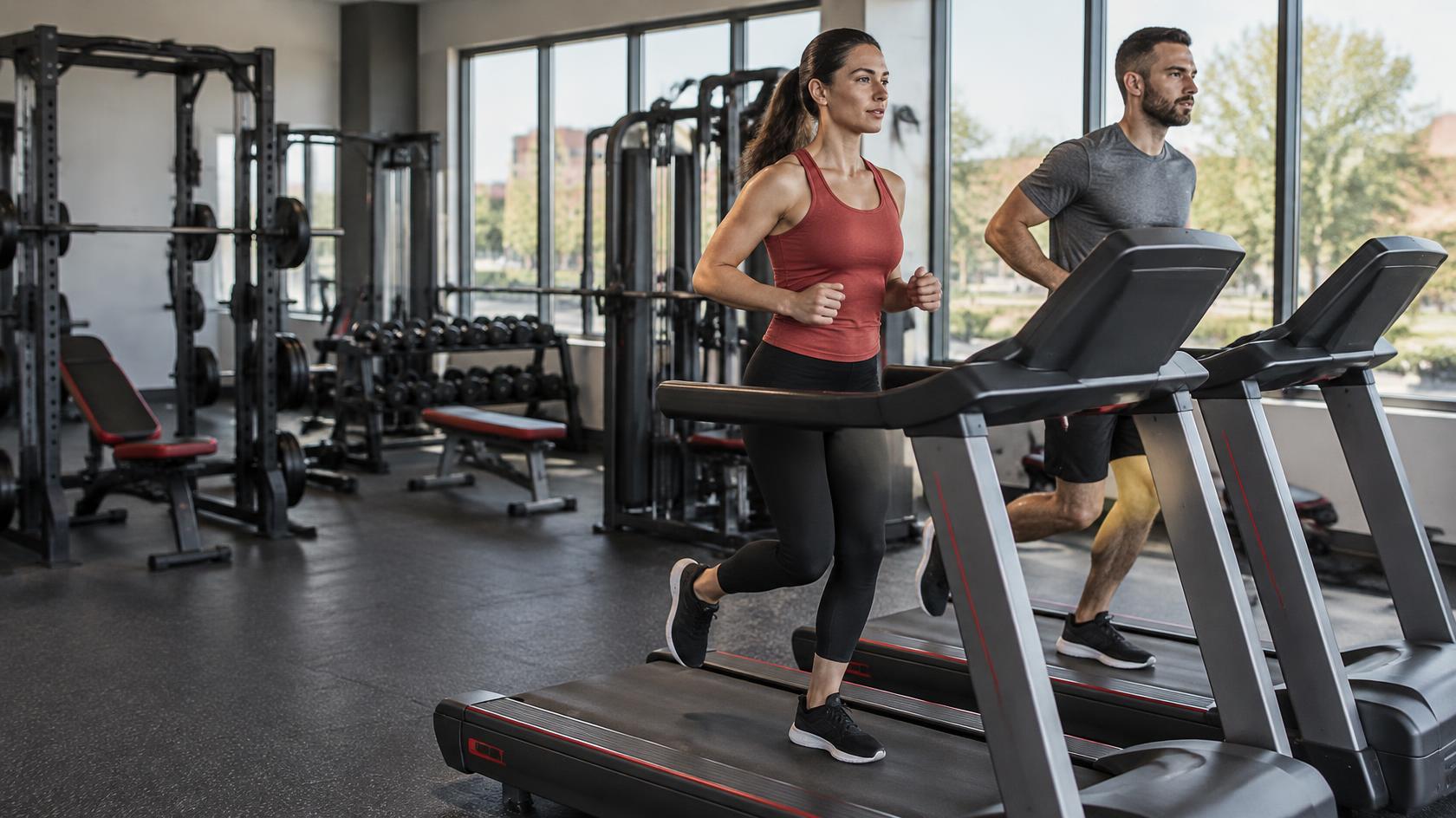 Two gym members running on treadmills in a bright neighborhood fitness center