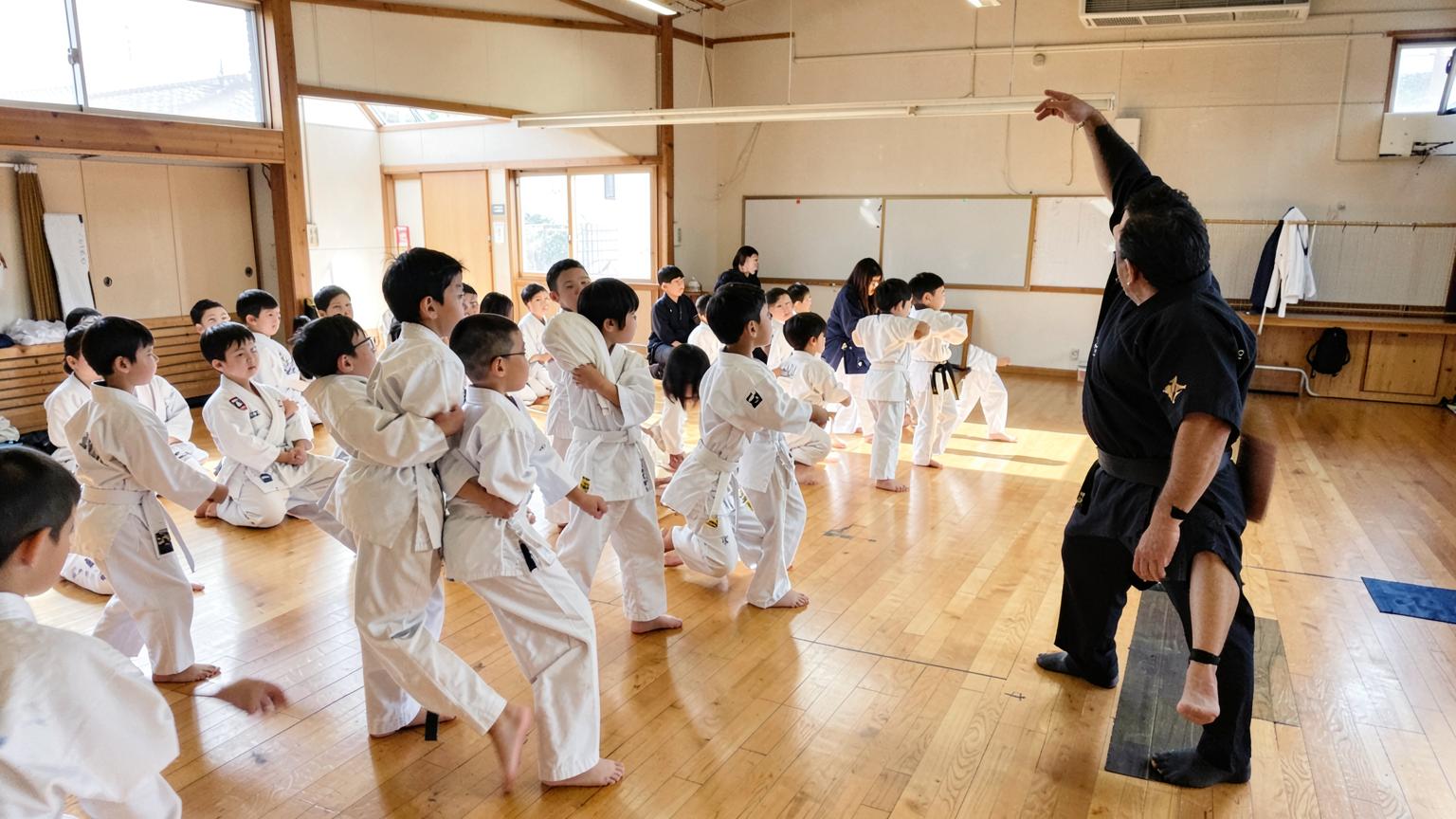 Children in white gi practicing kata while an instructor coaches