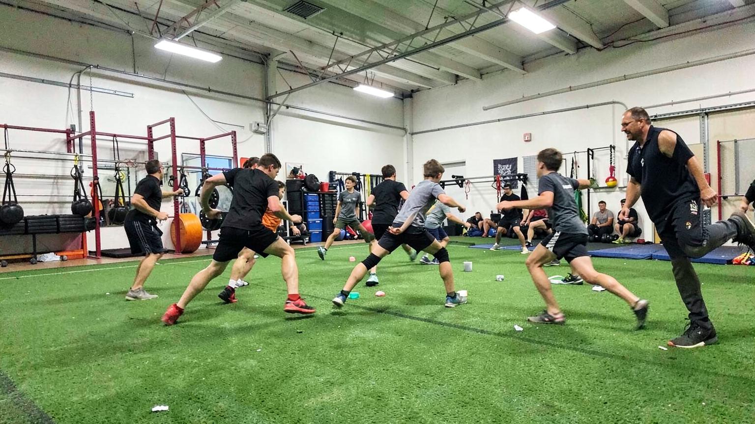Young athletes running agility drills on indoor turf with a coach